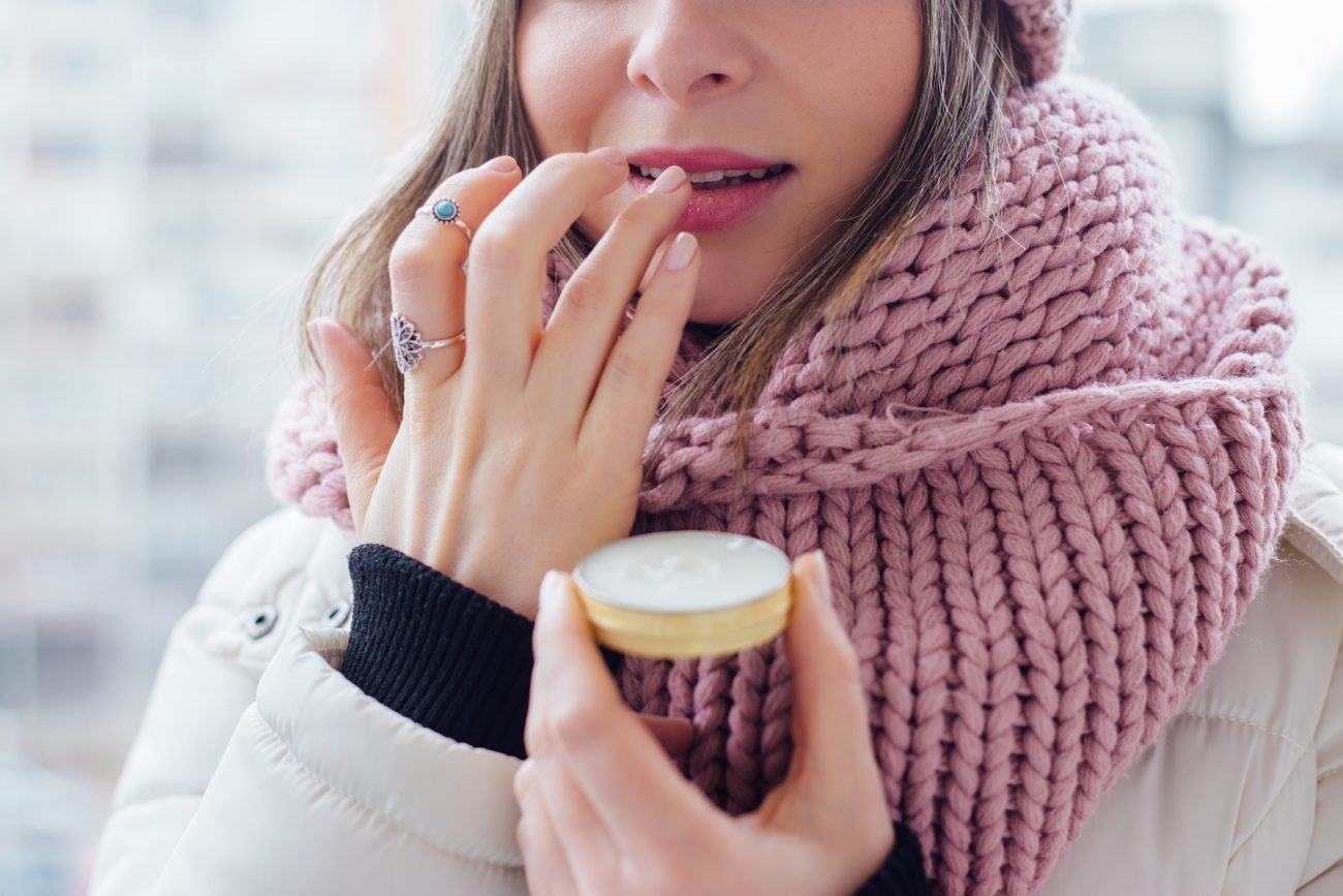 Mulher usando protetor labial para representar cuidados com lábio e skincare no inverno