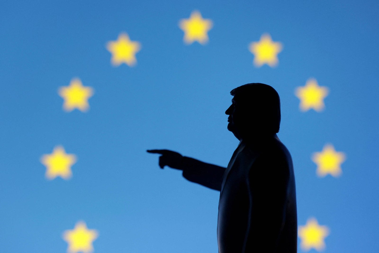 Sombra de homem de perfil apontando com a mão direita estendida, em frente a fundo azul com doze estrelas amarelas dispostas em círculo, representando a bandeira da União Europeia.