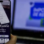 Celular e computador aberto no site oficial da Receita Federal, onde o CDB do Banco Master deve ser declarado no IR 2026.