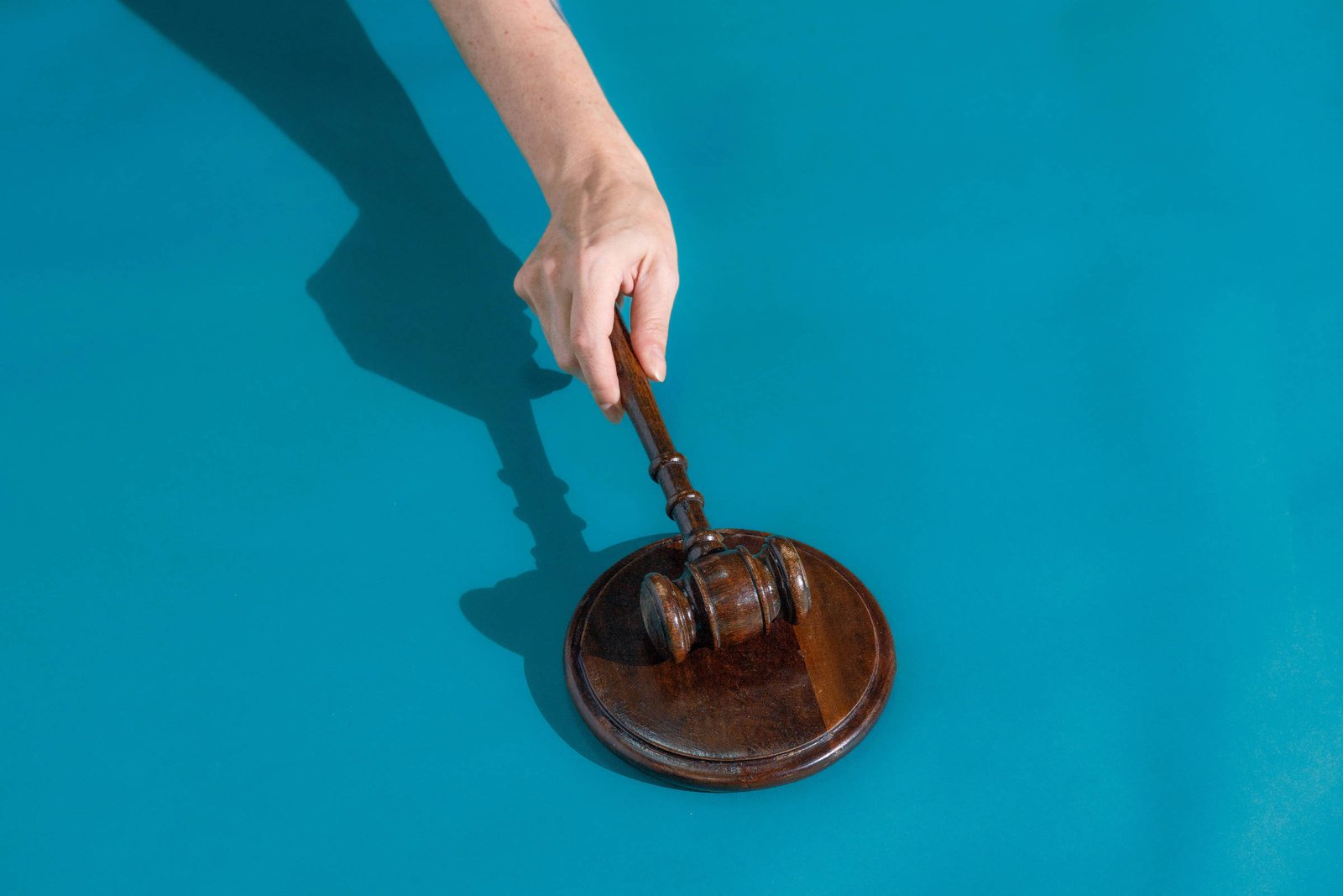 Mão de uma pessoa segurando um martelo de juiz (malhete) acima de uma base, prestes a bater, simbolizando decisão judicial, sobre fundo azul.