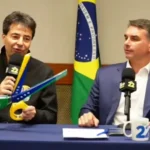 Sachsida segura tesoura com as cores da bandeira do Brasil que simboliza promessa de corte de gastos em live ao lado de Flávio Bolsonaro (PL)